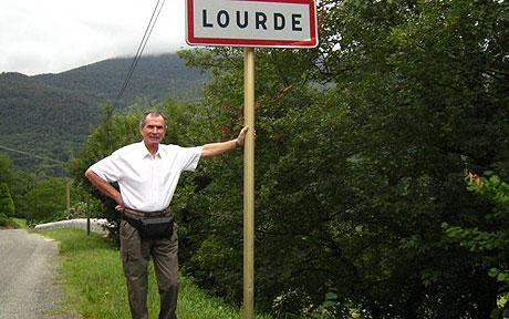 Photograph of a man standing at the street sign for Lourde in France.
